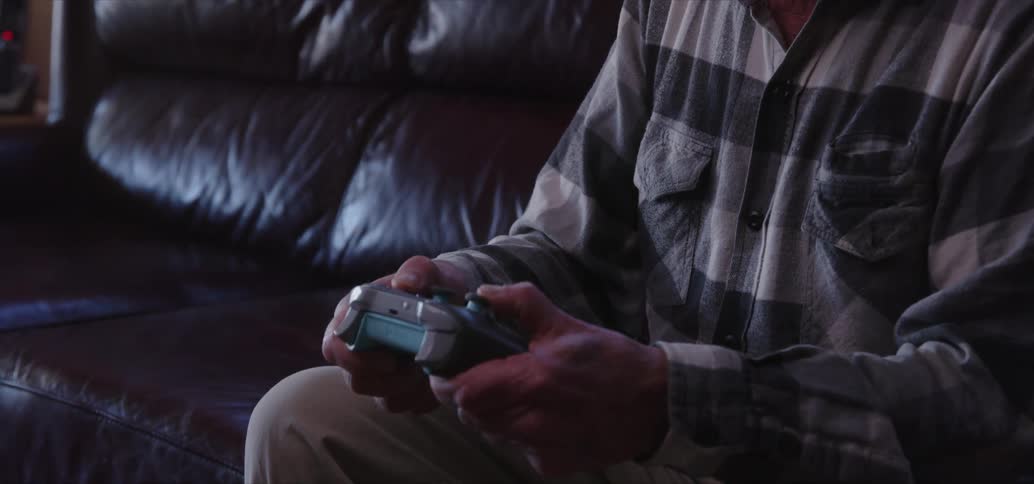 An elderly man playing video games sitting on a sofa
