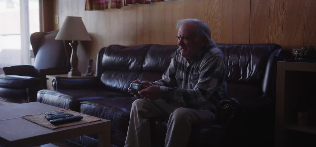 Elderly man sitting on a leather sofa having fun while playing video games