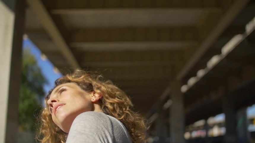 A woman looking around pillars from under a bridge and looking up at the sunny sky