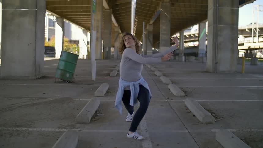 Woman moving rhythmically in a parking area beneath a bridge in slow motion