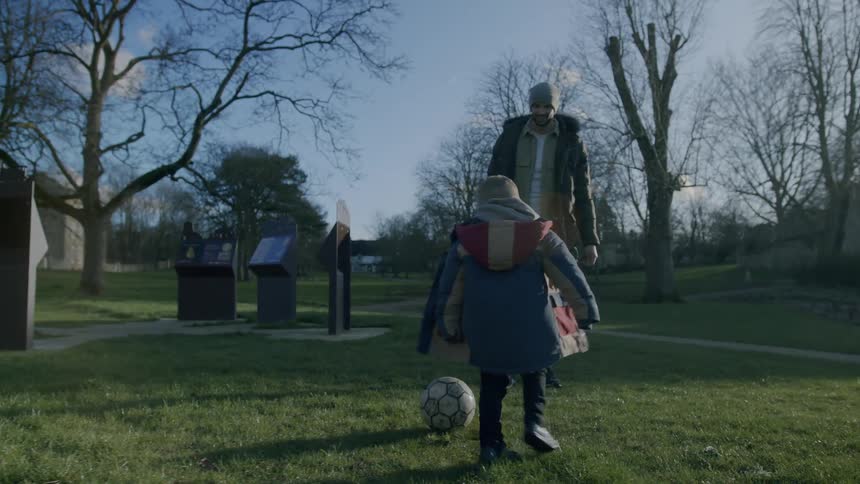 Father and son playing football in a park on a cold day