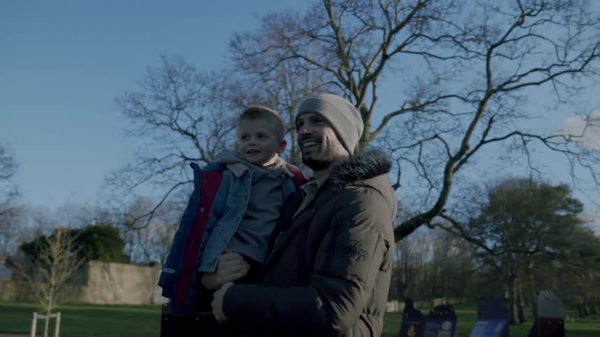 A man carrying a young boy in his arms shows him the park they are on