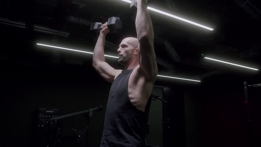 A man in a dark room working out with dumbbells