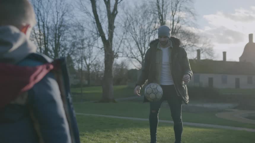 Father performing tackles with the soccer ball and his little son watching