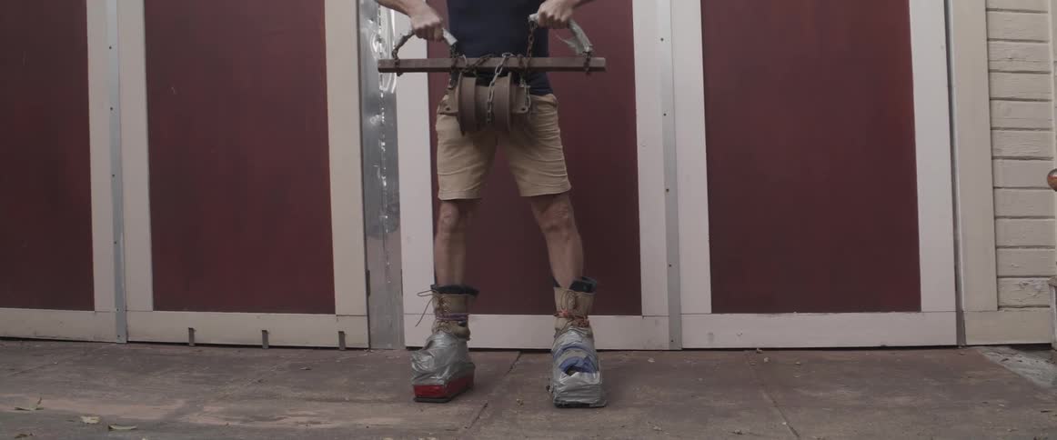 Elderly man wearing makeshift shoes lifting a weight in the backyard