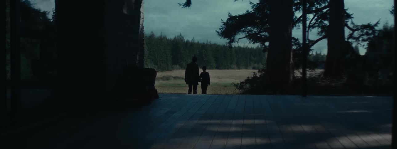 A woman and her daughter walk away from wooden platform toward field as lightning brightens dark clouds over nearby conifer forest