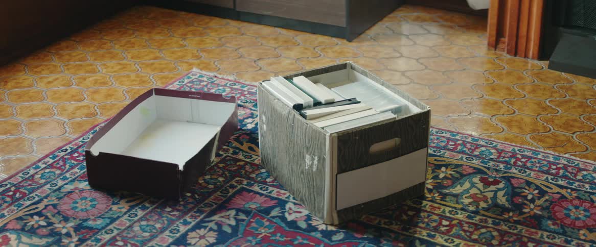 A full cardboard file box sitting on an area rug with its lid off and lying next to it