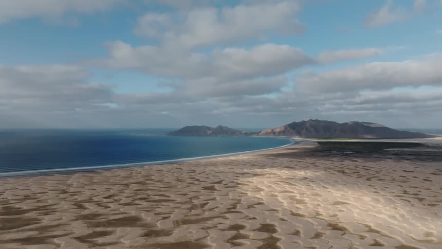 Flat beach and mountains border ocean under a cloudy sky