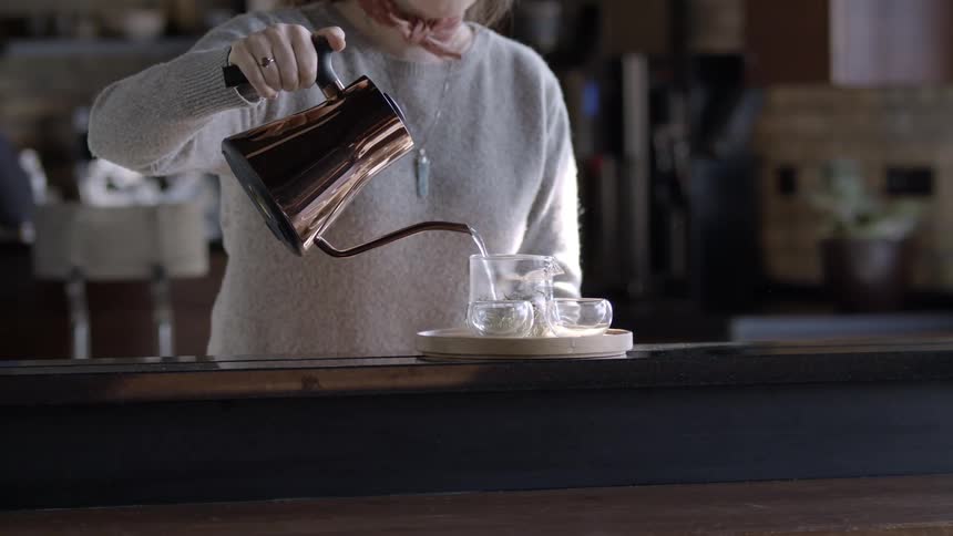 A woman pouring water into a mug to make a cup of tea