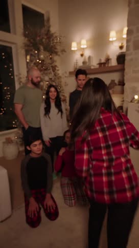 A woman is looking forward while packing something and then runs to the back where there is a whole family happily hugging each other and posing