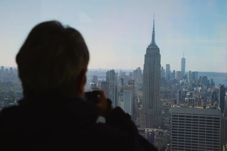 Man take pictures of the city buildings while standing indoor at midday