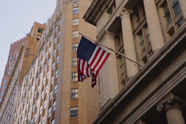 An american flag waving in the wind hanging from a flagpole on a building