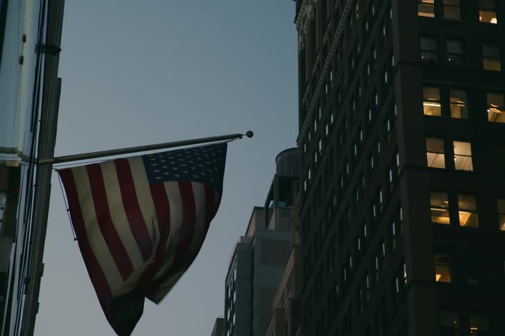 American flag waving in the wind mounted on a pole in front of a tall glass and steel office building