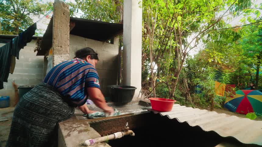 Woman in the backyard washing clothes with soap on a stone