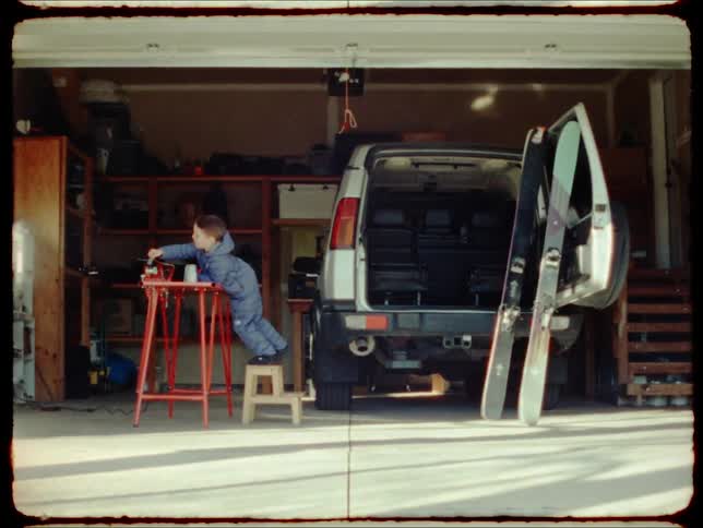 A little boy uses a step stool to reach an object on a folding table