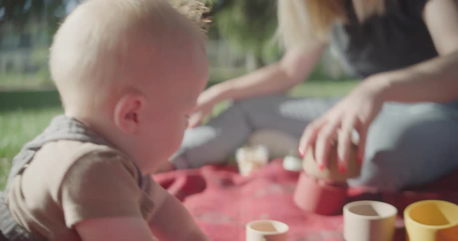 Mother and son on a picnic outdoor while the baby plays with cups