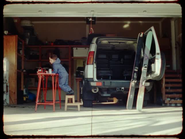 Little boy heading towards the garage climbing on a small stool and resting his arms on a table with a machine