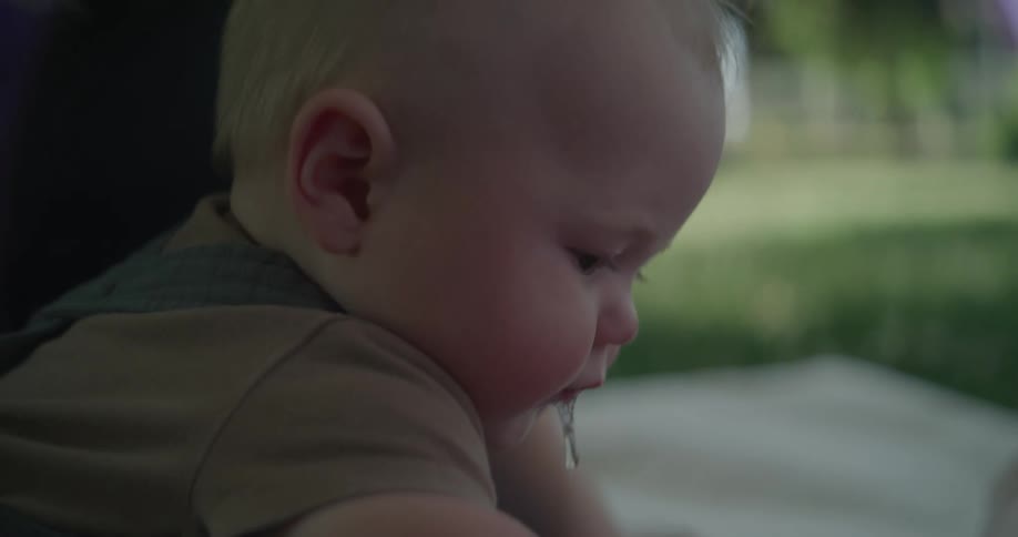 A baby is seated outdoors with an adult while playing with toys