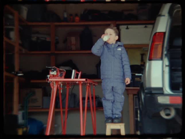 A young boy in a garage takes a drink