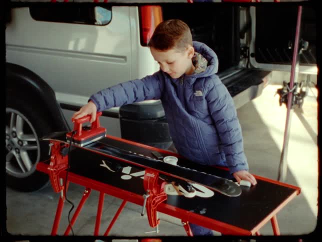Little boy passing a press machine over a piece of wood in the garage