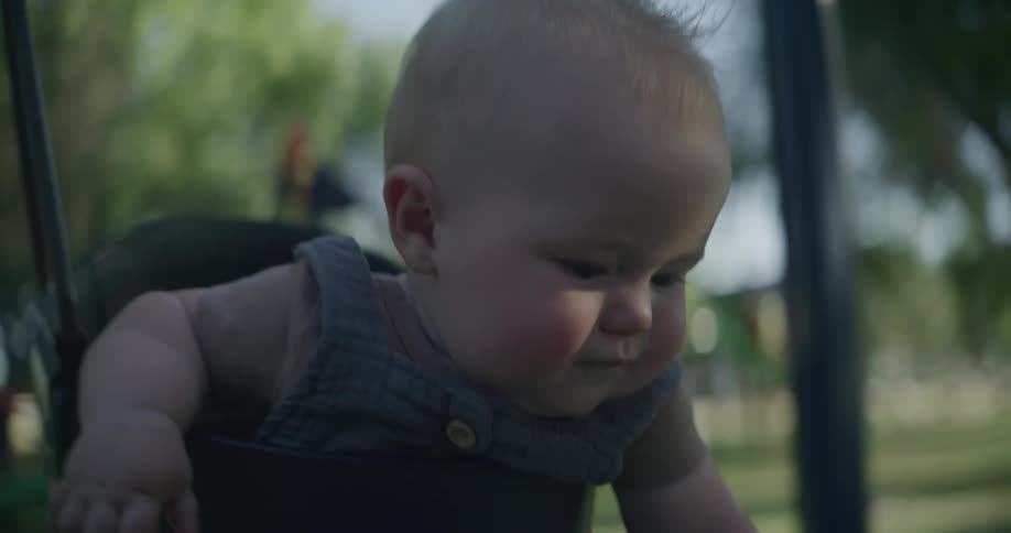 A cute baby with drool on its chin smiles while in a swing