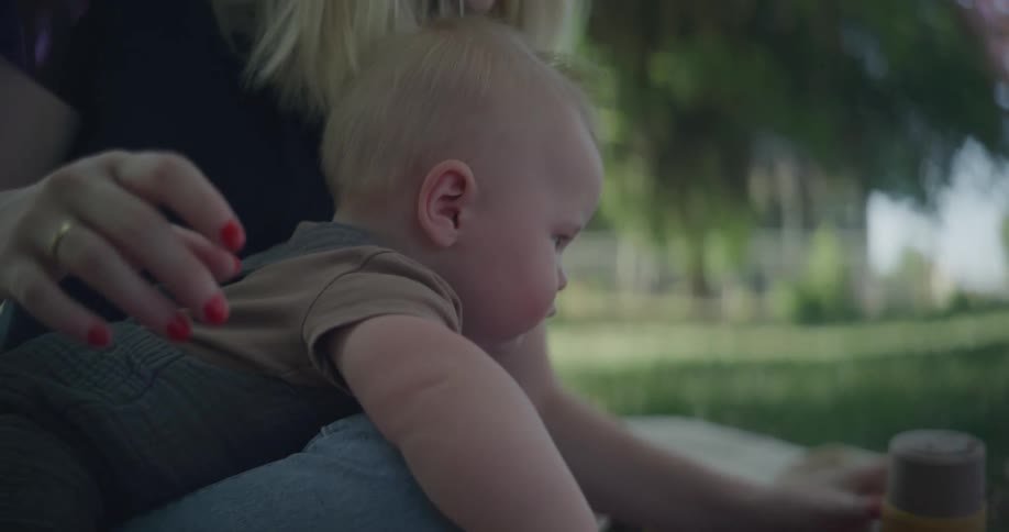 A mother sits in a park while her baby reaches for toys to play with
