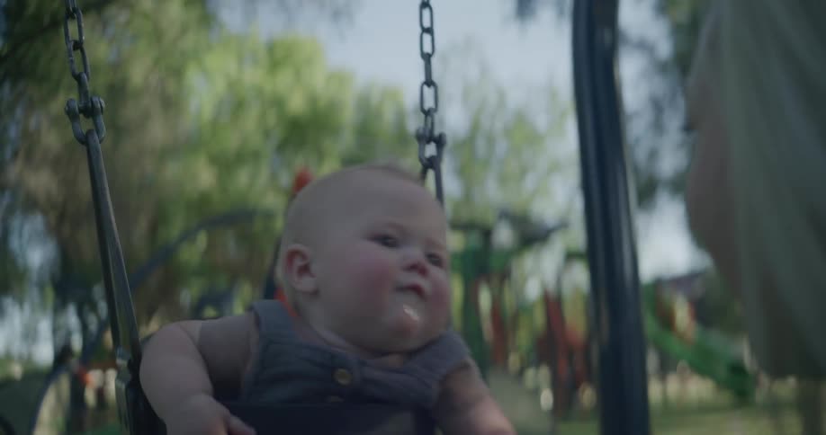 Mother pushes her baby in a swing at the park