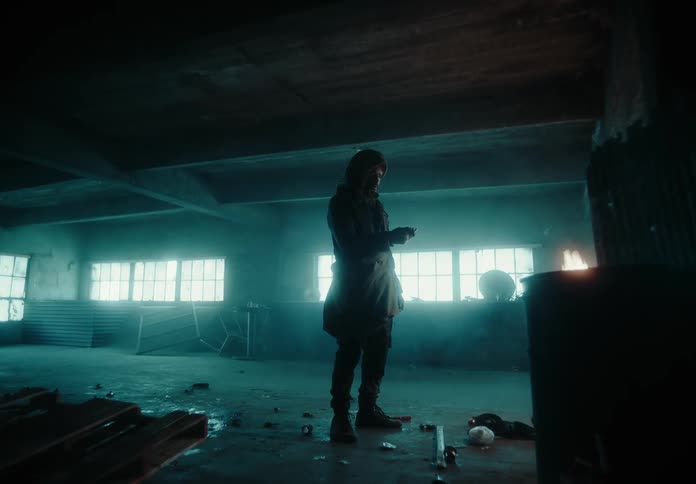 A man walks into a run down factory room where an open fire burns