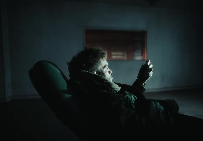 A lone man sits in a reclining chair in a room with a flickering light source