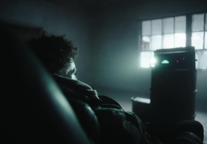 Man in a cold room sitting in an armchair and facing an abstract machine
