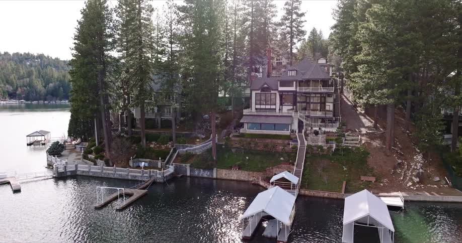 A large home sits at the waters edge in a forested area