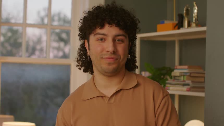 Man with curly hair stands in the living room looking at the camera
