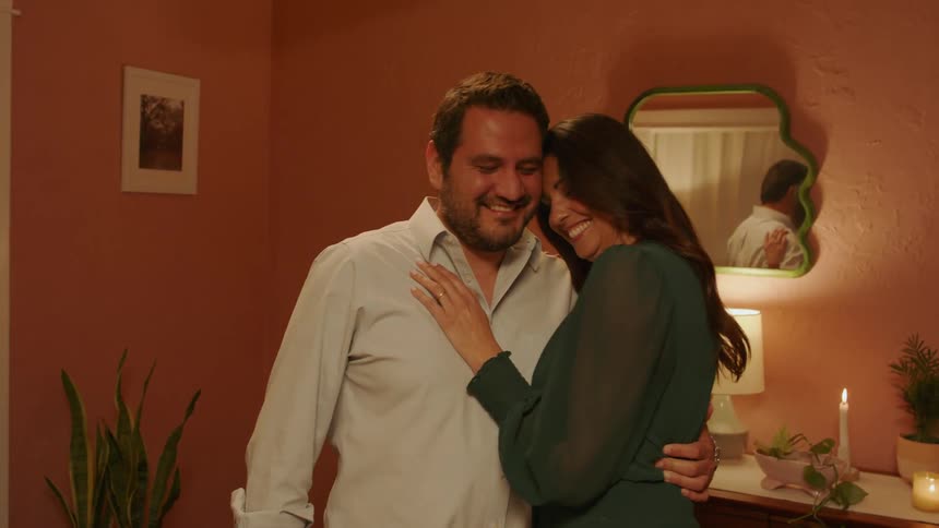 Man hugs his wife indoor while smiling at each other