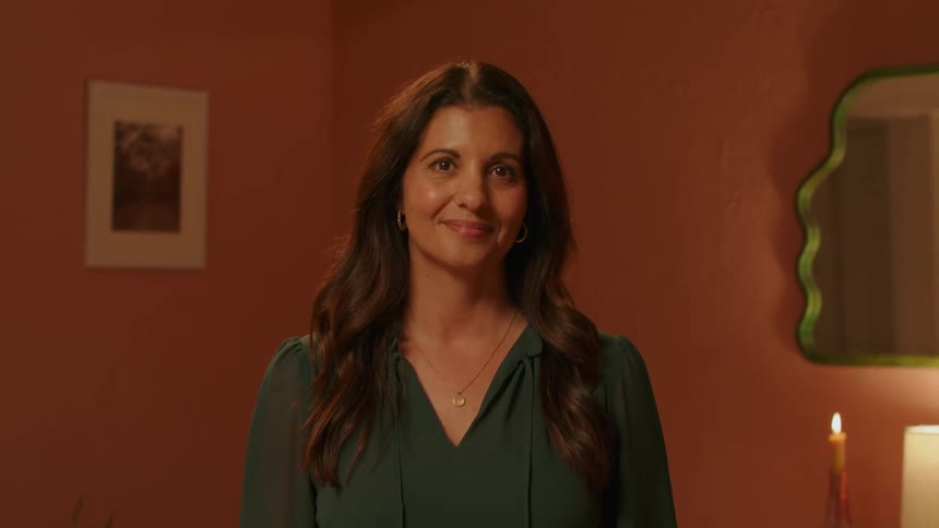 A woman stands looking straight ahead and smiling