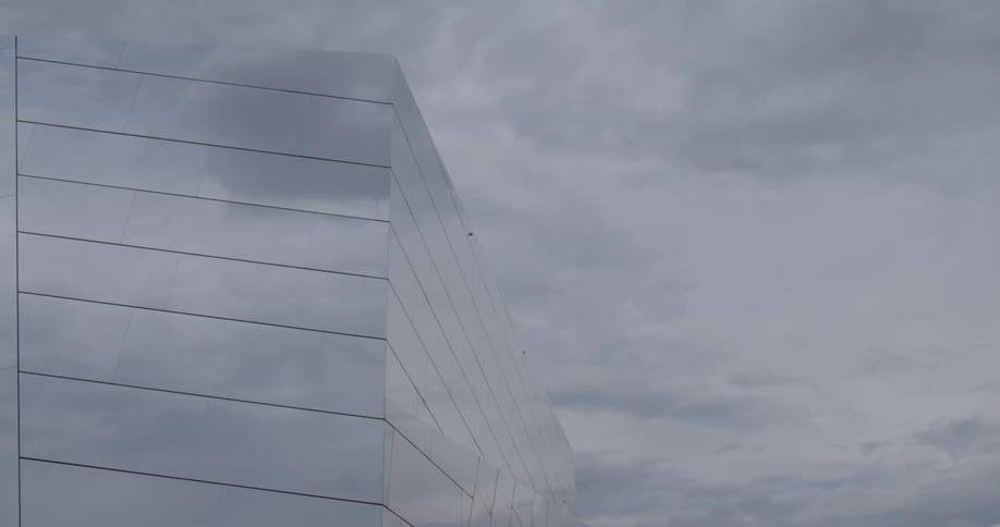 Clouds reflect on the mirror facade of a building hiding it in the sky