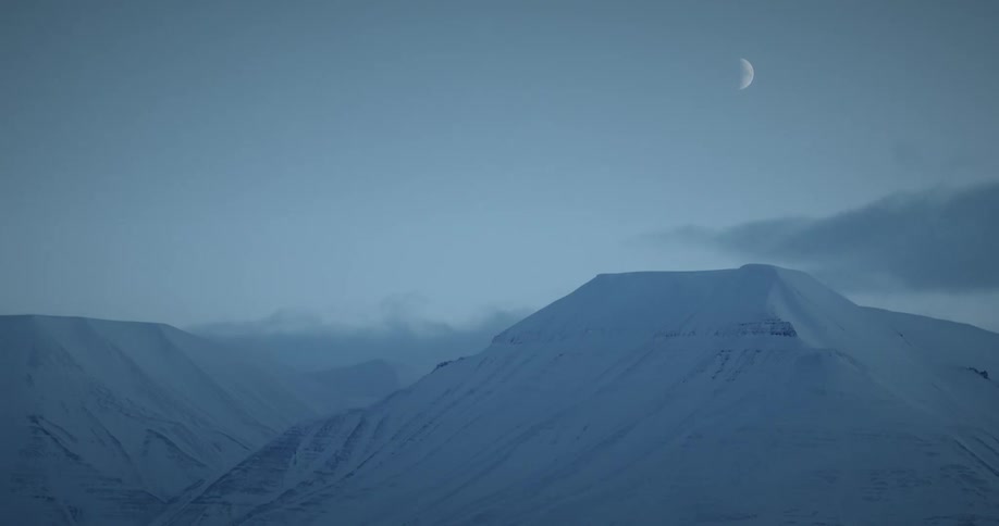 View of snowcovered mountains with passing clouds and the moon in the sky
