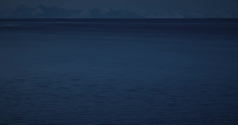 Aerial view of a body of blue water and distant snowy mountain range