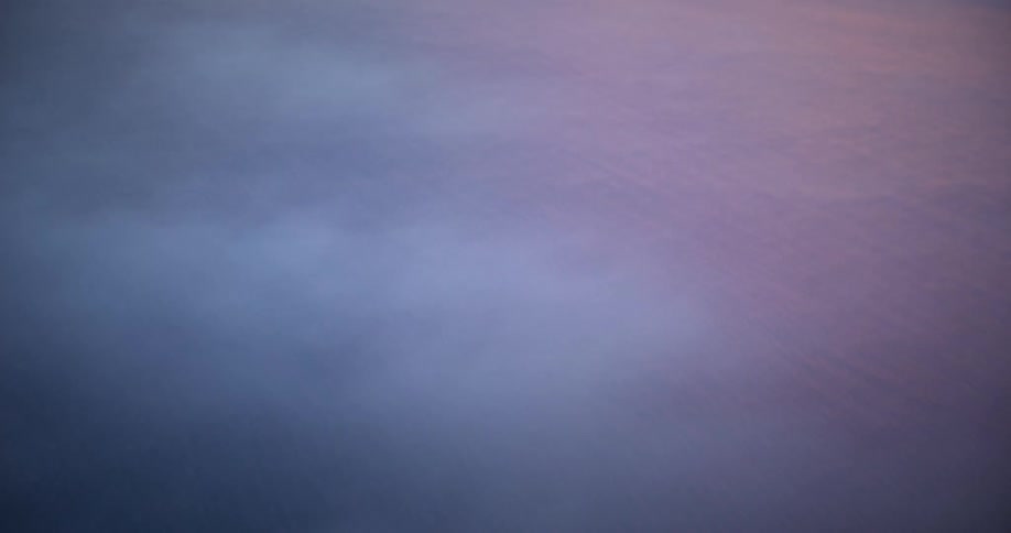 An aerial view over the ocean with cloud cover at sunset