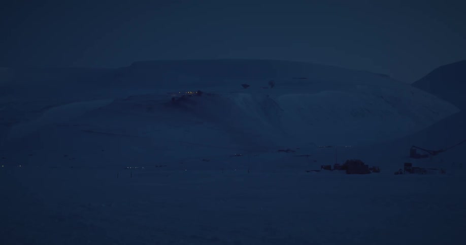 Lights from houses on and near mountains twinkle against the snow at night