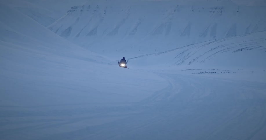 A person drives a snowmobile in the snow in between mountains