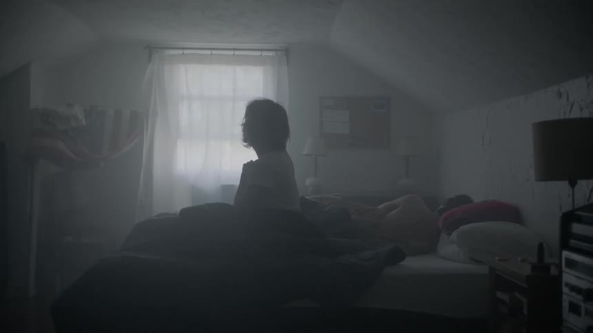 A woman sits up in bed and looks around pensively