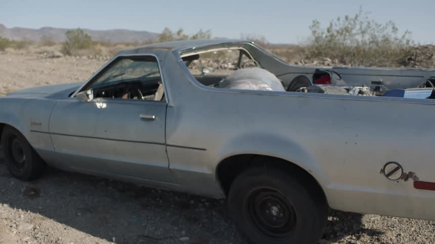 An old el camino loaded with junk is parked in a desert location