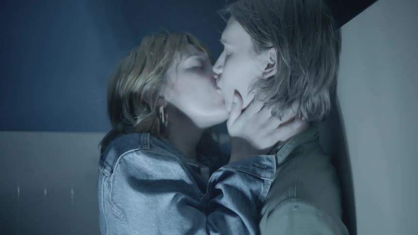 Two people kiss in a room with flashing lights