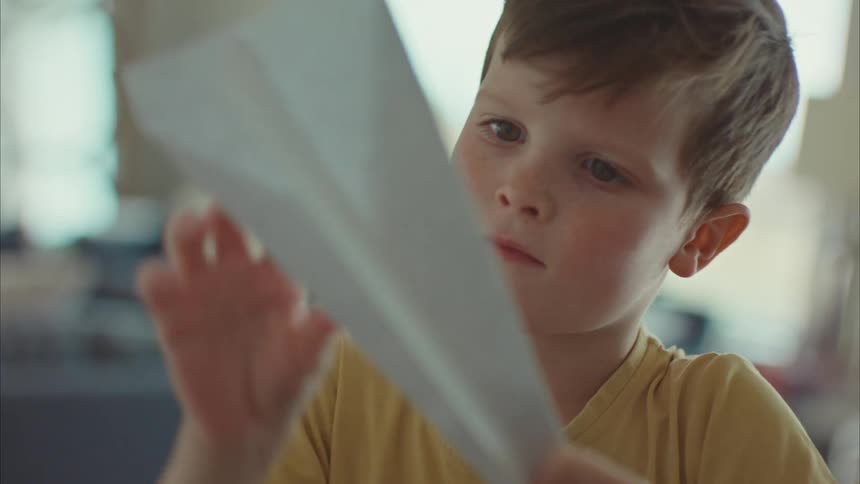 A clip of a boy making an airplane with paper