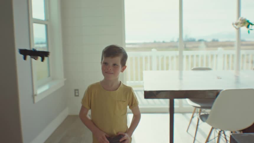 A young boy plays with a remote controlled airplane in a dining room