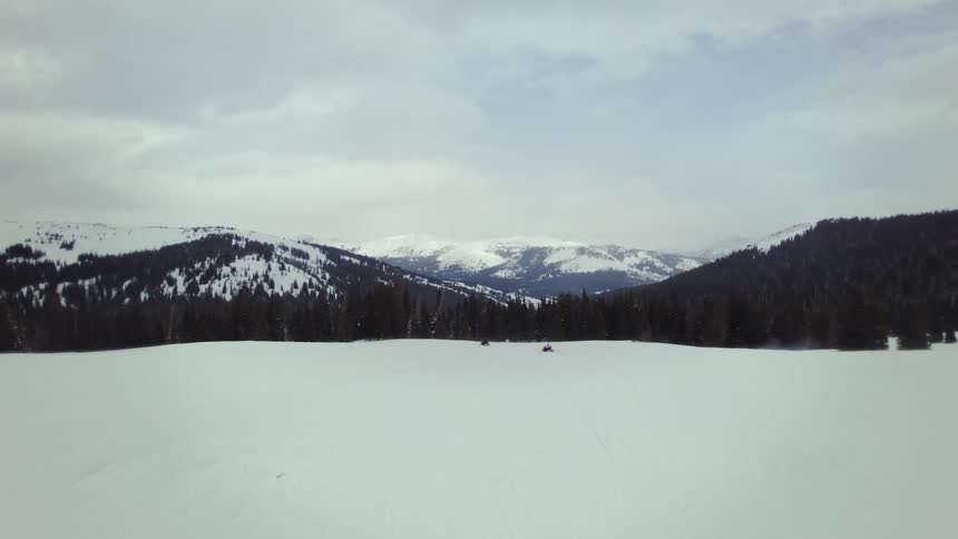 Aerial panorama of snowmobile traveling through mountains covered with snow and conifers