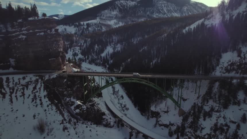 Aerial panorama of a bridge connecting mountains with forests and covered in snow