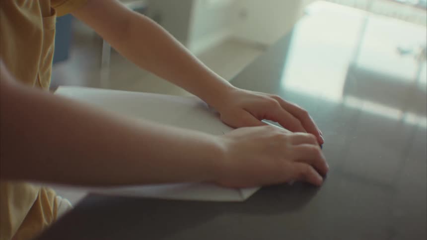A child folding paper on the table at midday