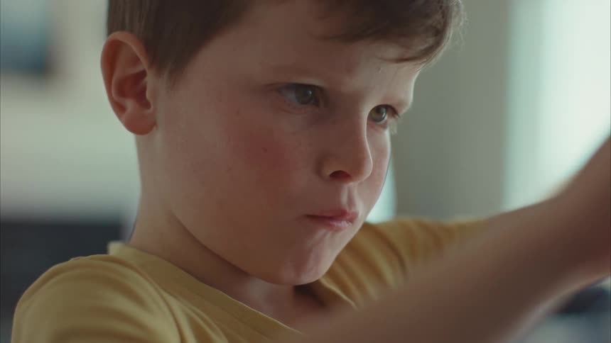 A boy child folding a paper indoor while standing at midday