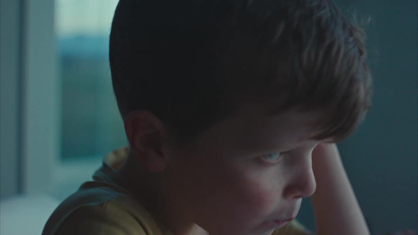 Boy sits at home near window eating cereal